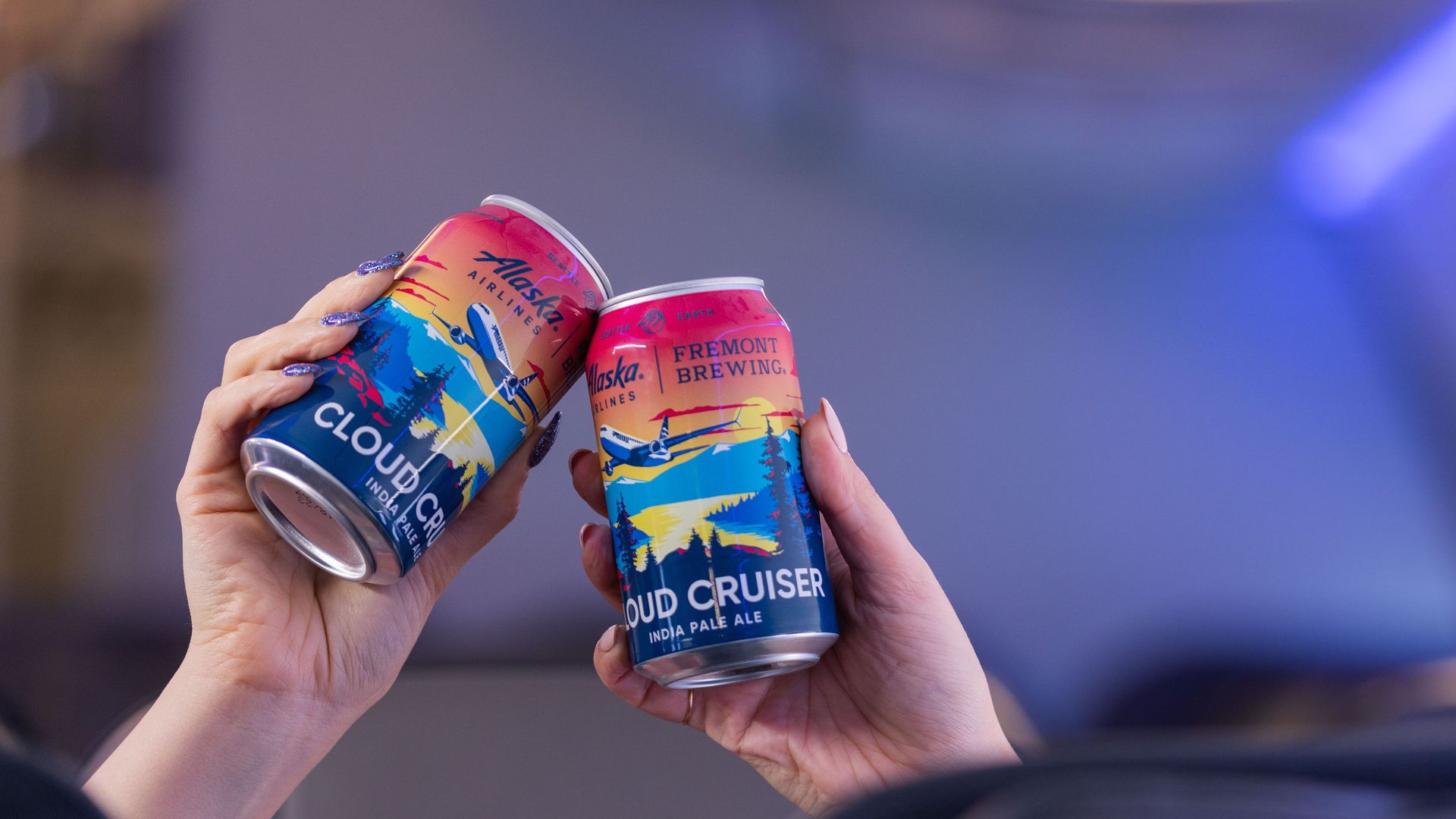 Two hands clicking colorful beer cans together in a toast.