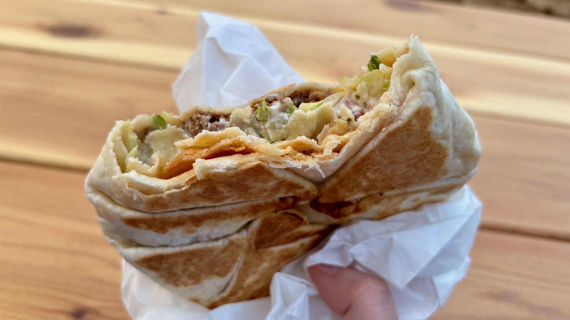 A close-up of a local version of Taco Bell's Crunchwrap, held in a white wrapper.