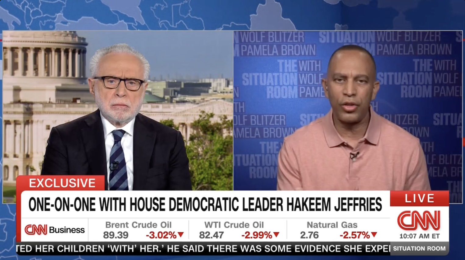 Split-screen CNN interview: left, older man with white hair and glasses in a dark suit; right, man in a pink polo against a blue "The Situation Room" backdrop. EXCLUSIVE banner with stock ticker.