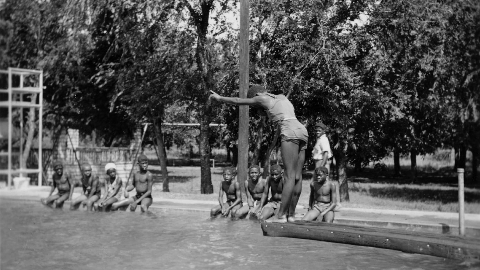 A kid is on a diving board while other kids look on.