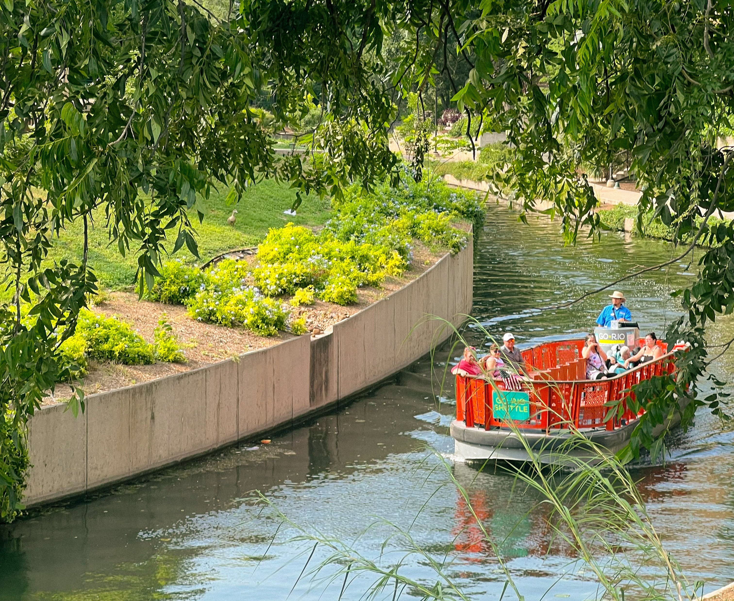 A red river barge cruises through the San Antonio river on a sunny day. 