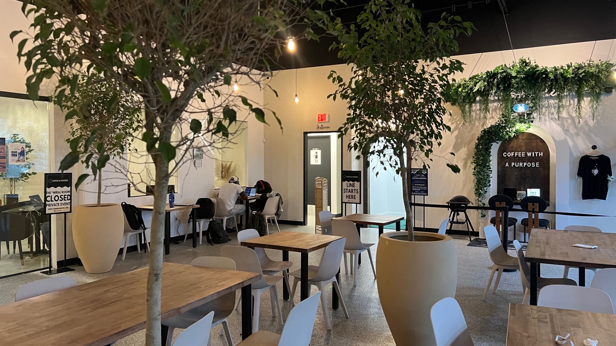 A photo of a coffee shop with beige tables and green trees 