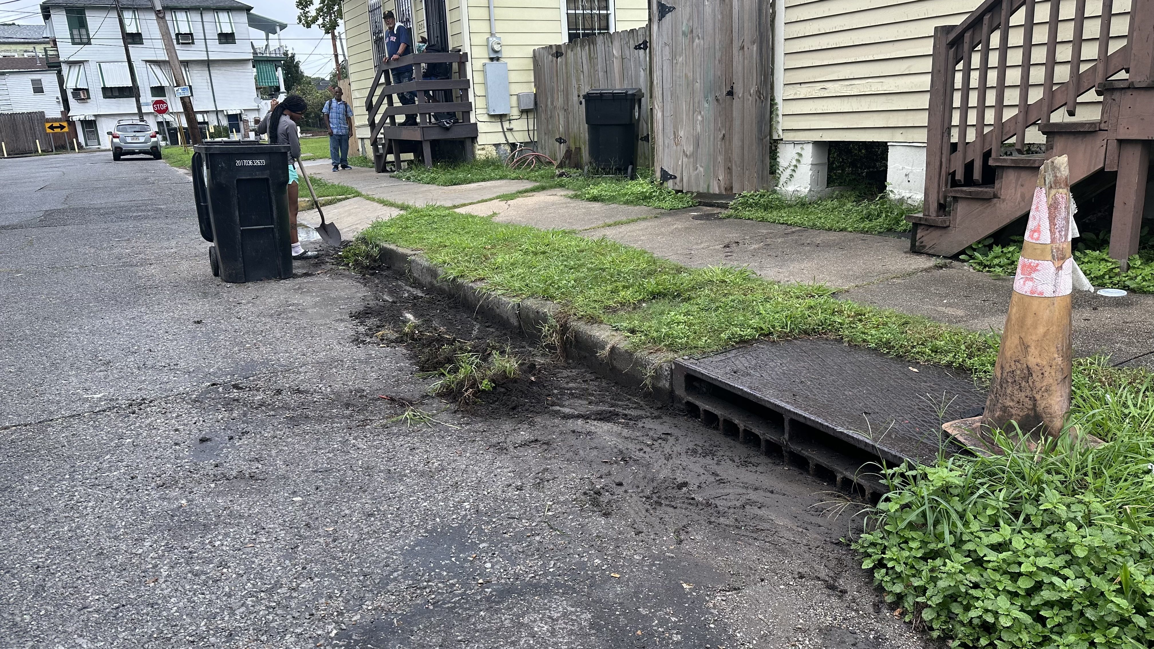 A young woman scrapes the street with a shovel as she clears the front of a storm drain.