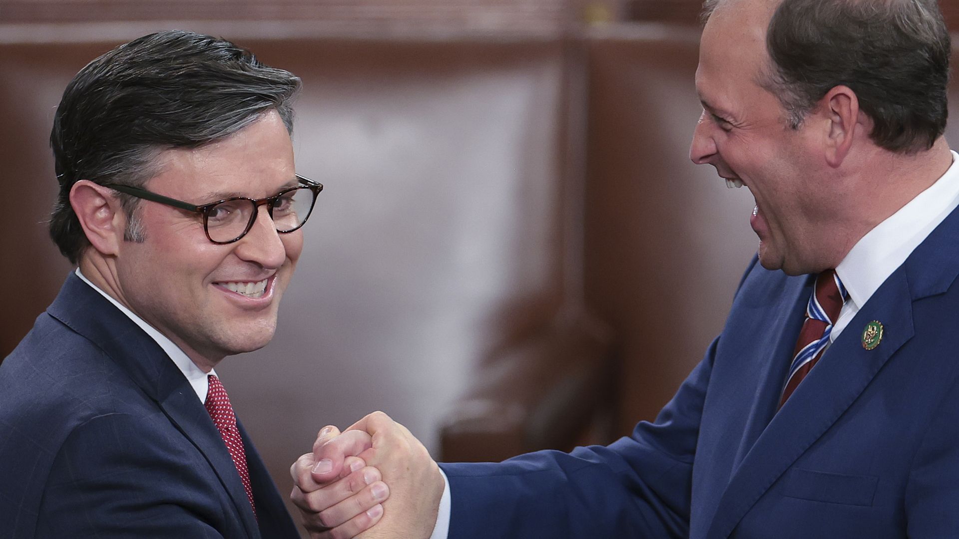 Two men in suits clasp hands in excitement.