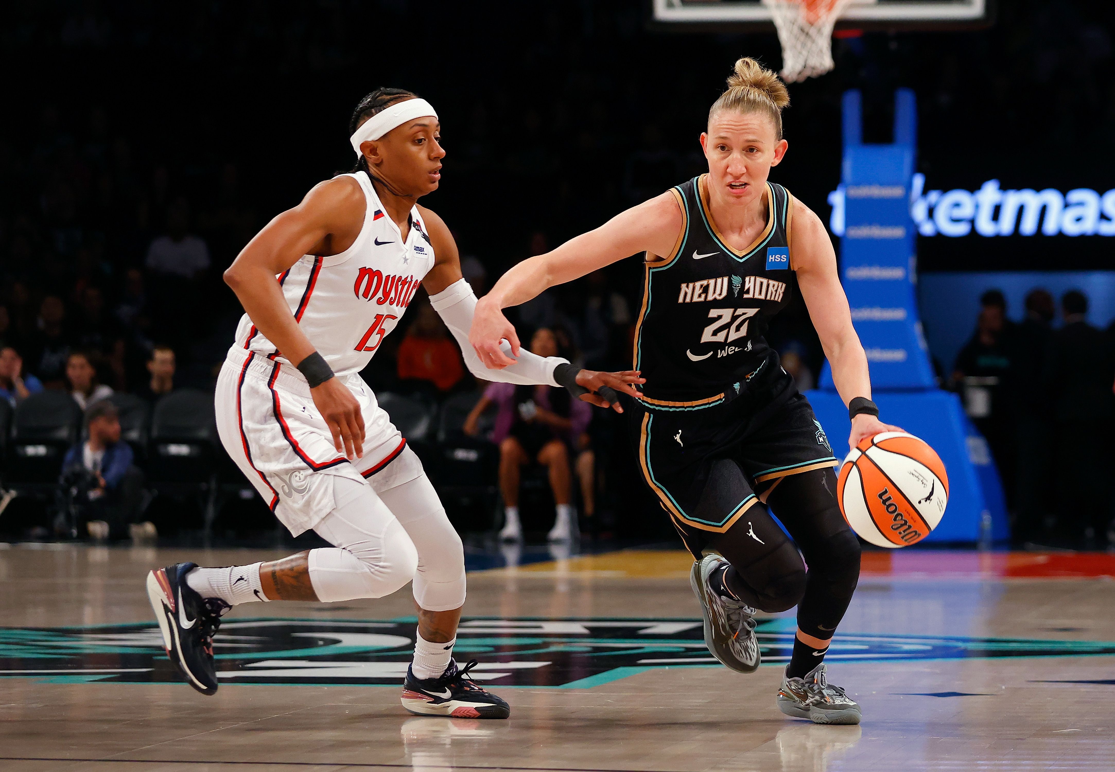 A woman in a black jersey dribbles a basketball past the defense