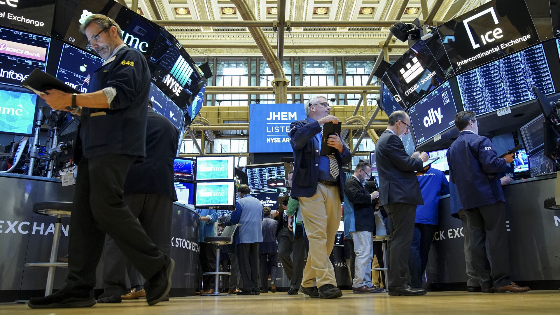 In this image, the camera looks up from the New York Stock Exchange floor as men walk across the floor and look at screens.