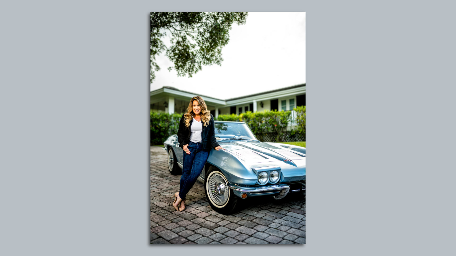 Lissette Calderon wears heels, jeans and a blazer while leaning against a vintage Corvette Stingray 