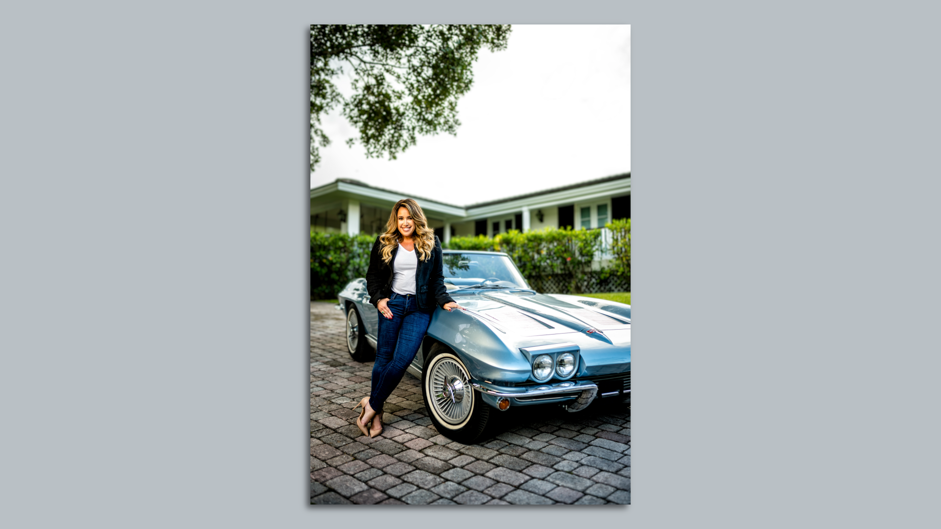 Lissette Calderon wears heels, jeans and a blazer while leaning against a vintage Corvette Stingray