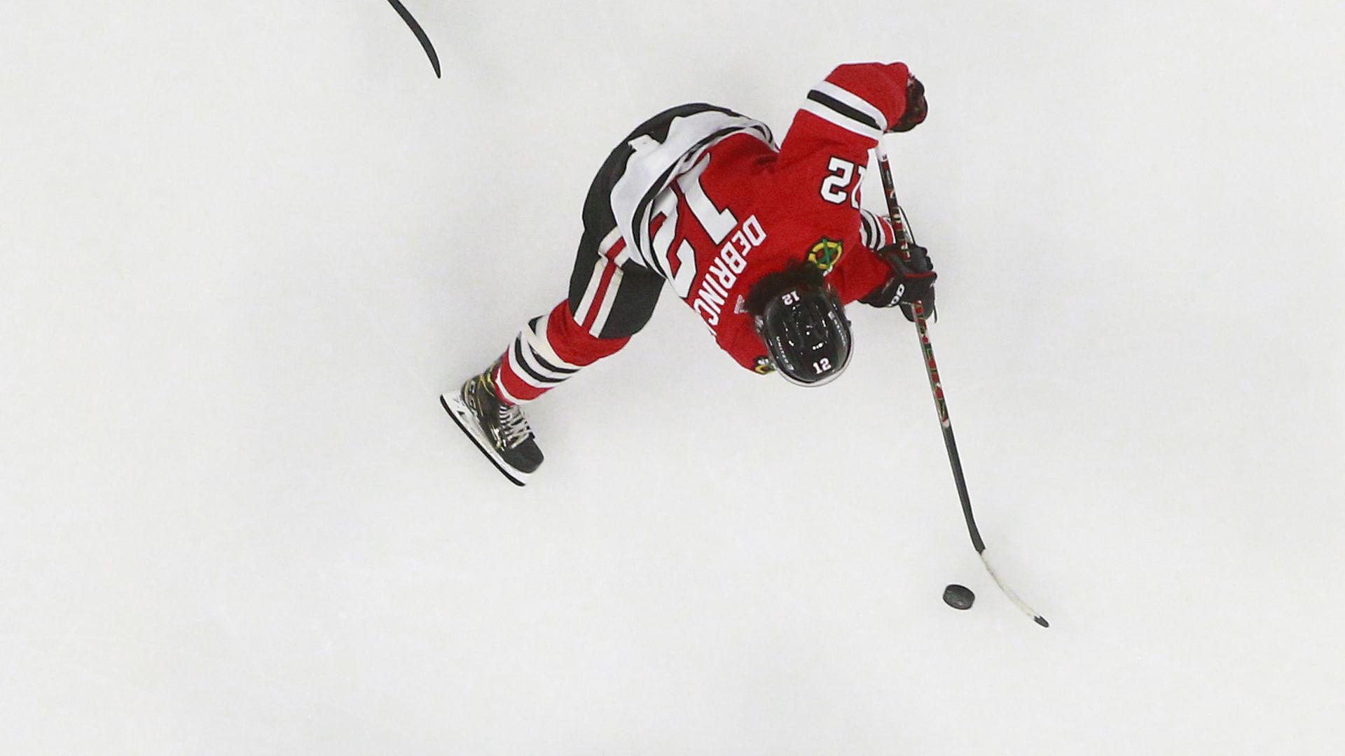 Photo of a hockey player in red facing off against a hockey player in green on ice