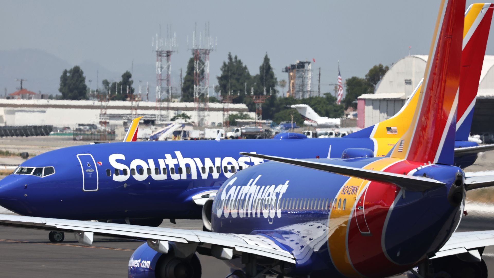 Two Southwest Airlines planes with blue, red, and yellow colors parked on an airport tarmac with buildings and communication towers in the background.