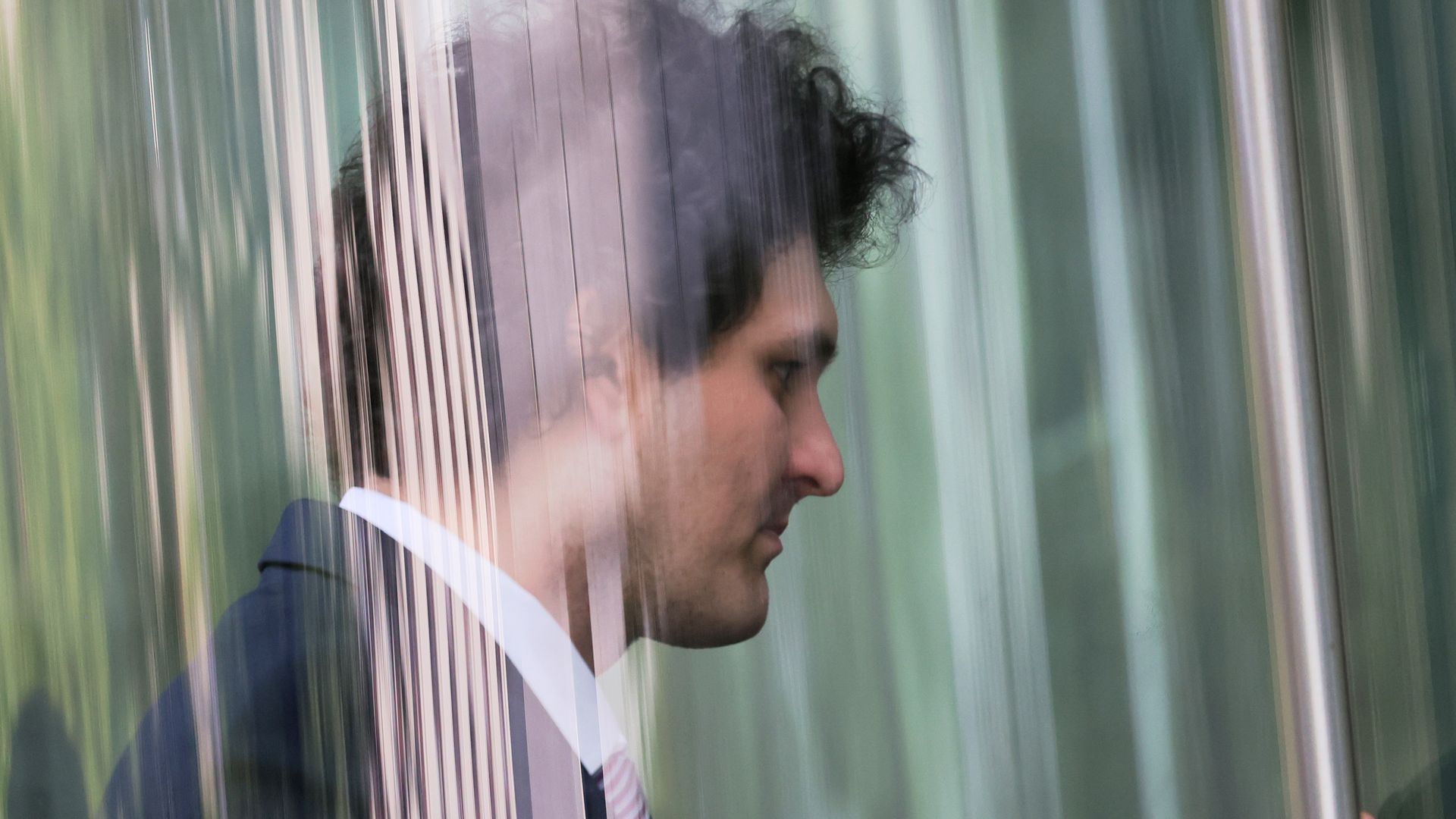 A young man entering a building, passing through glass doors. 