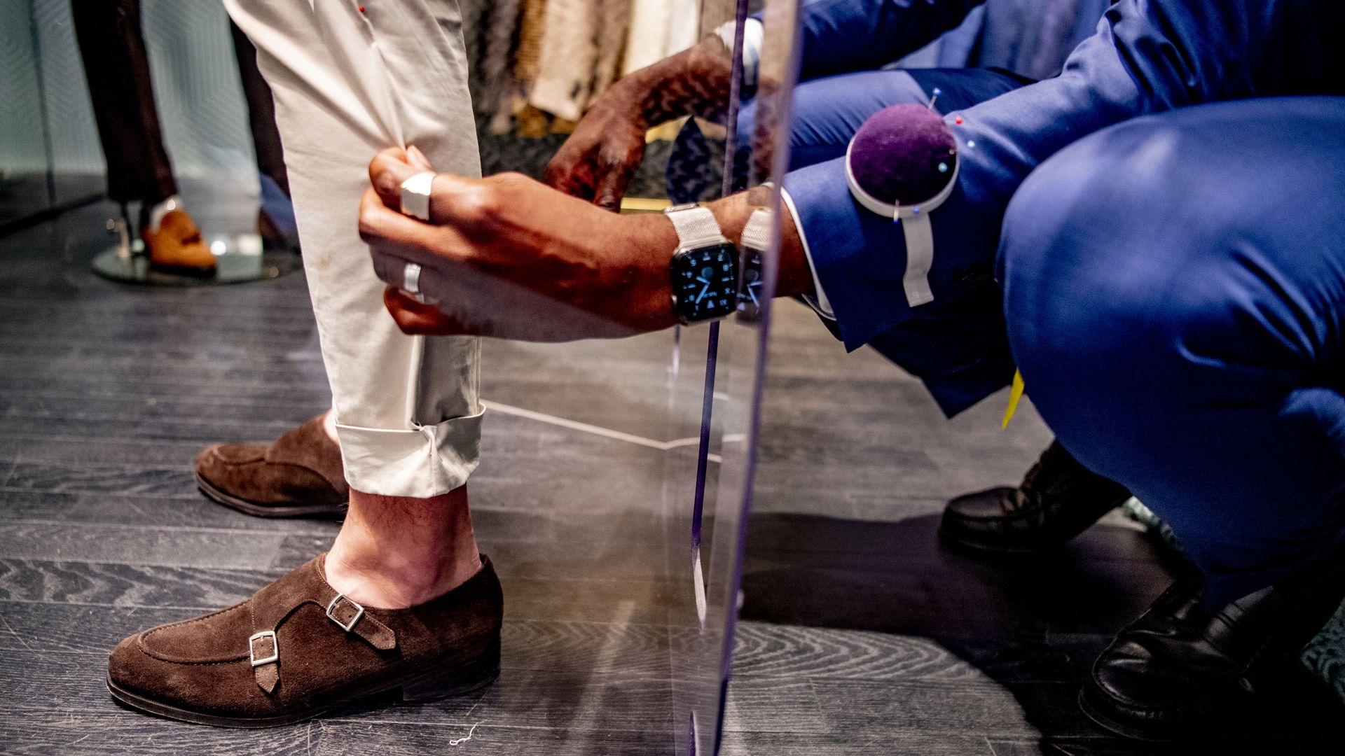 A tailor makes adjustments to a suit through a plexiglass divider.
