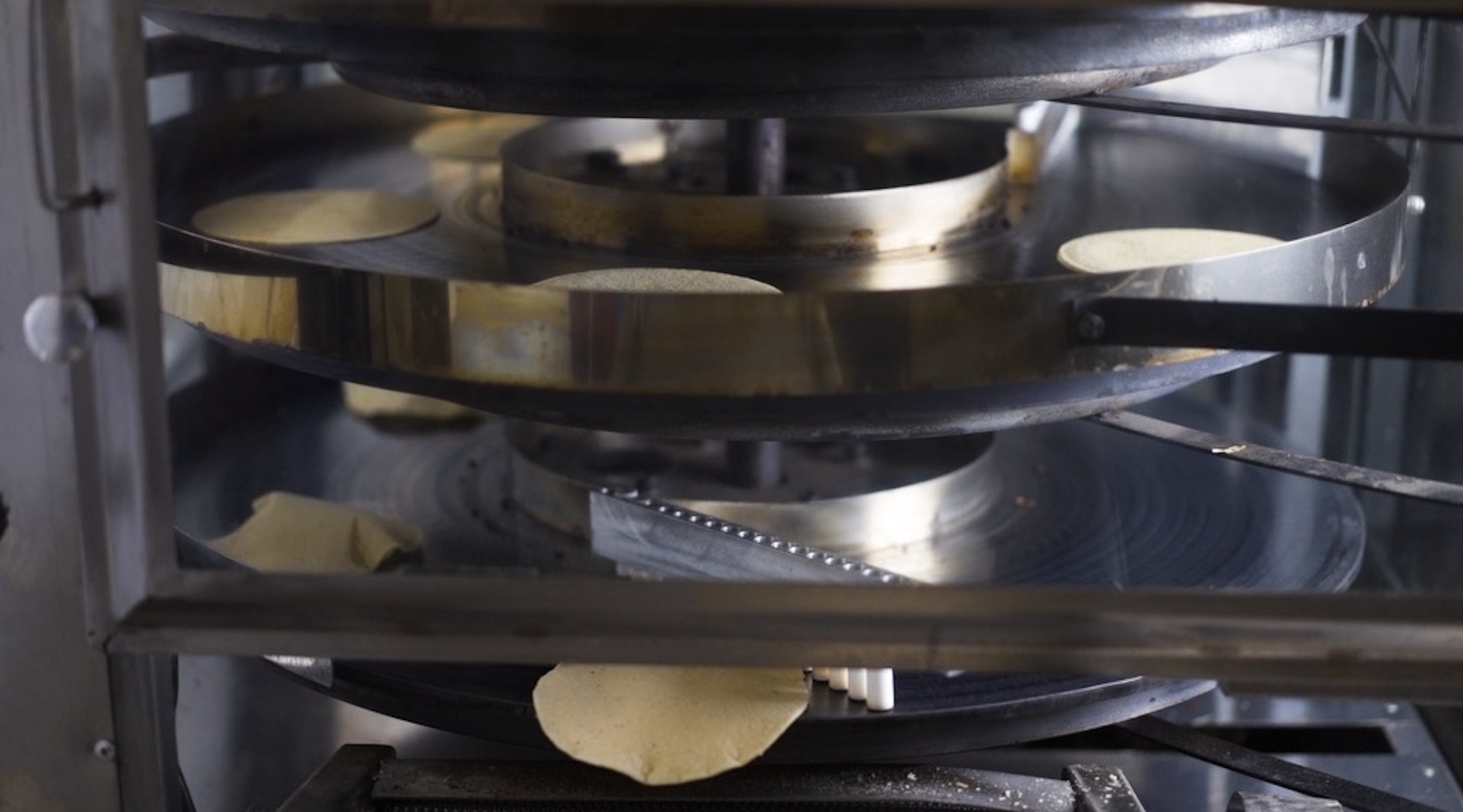 Tortillas cook on a machine.