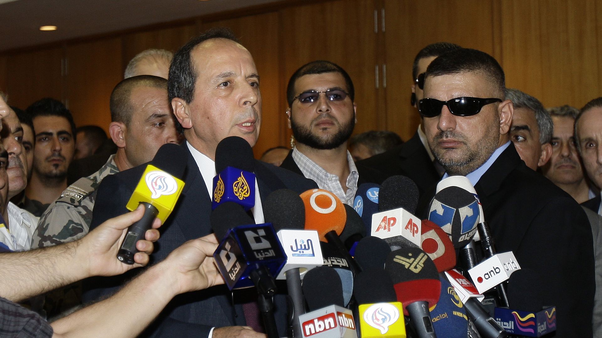 Photo of Jamil Sayyed with a crowd of people around him putting microphones in his face