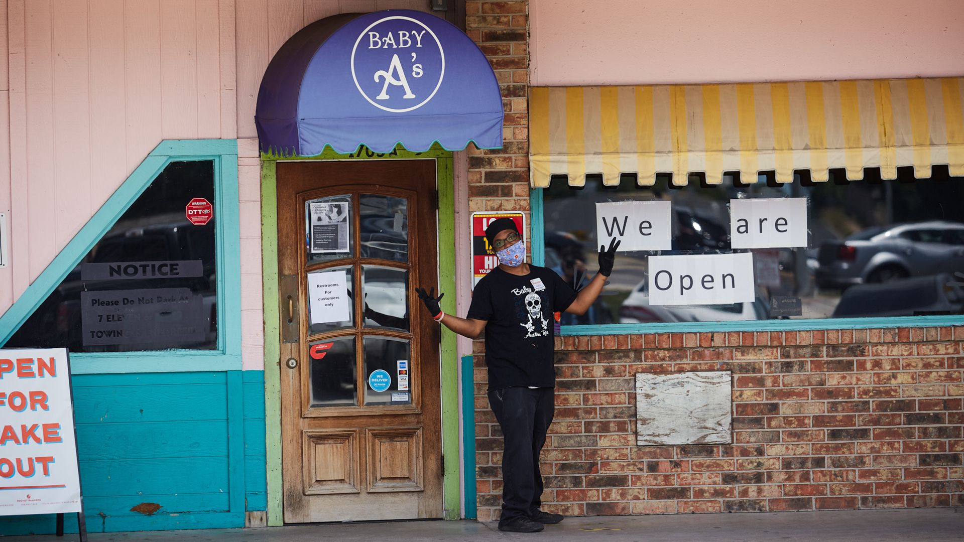 In this image, a masked person stands next to a sign that reads "we are open"
