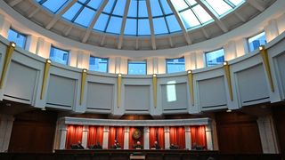 Judges in robes and face-masks sit underneath a circular window during a hearing at the Ralph Carr Judicial Center in Denver. 