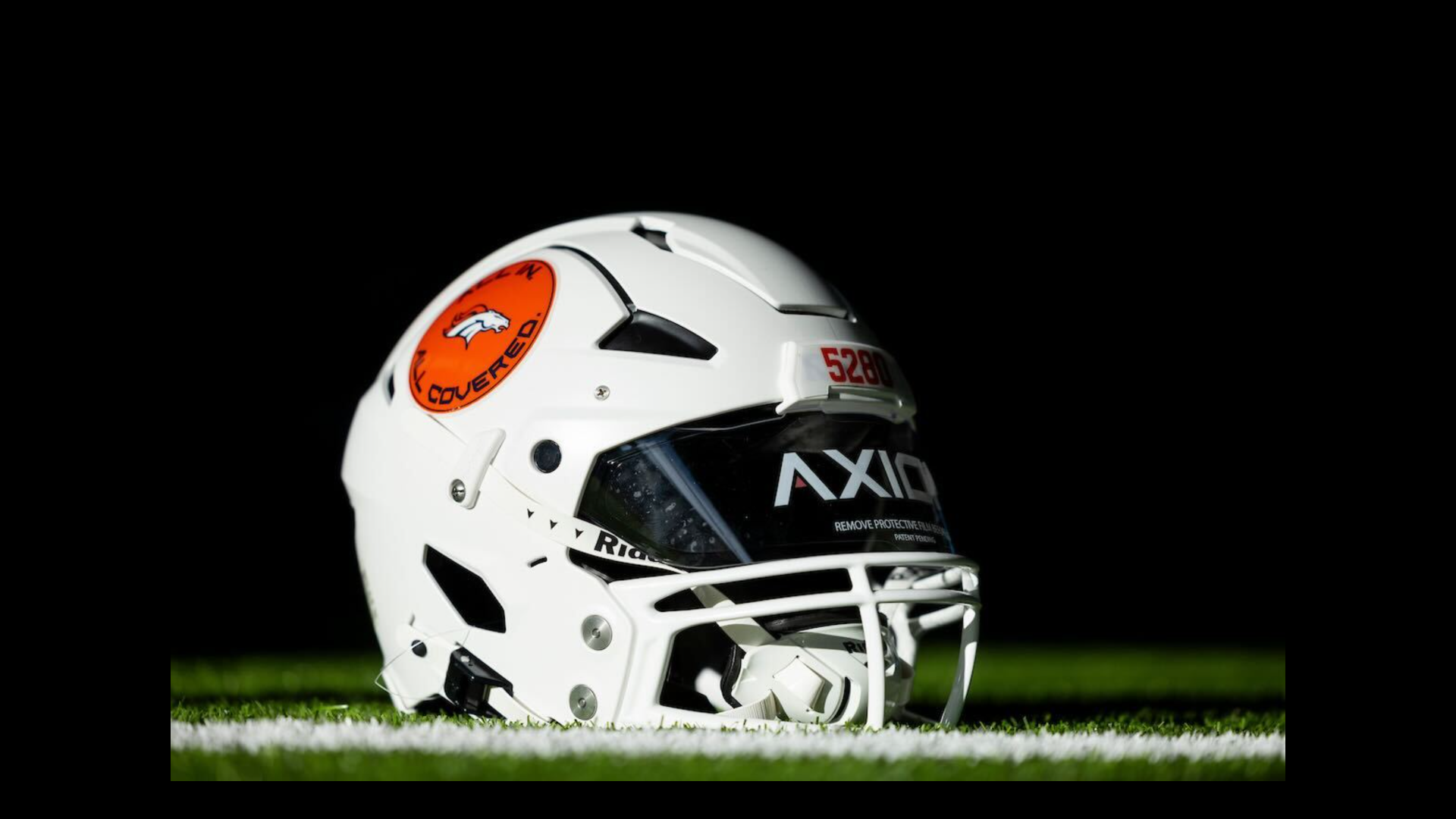 A white American football helmet with a bright orange sticker.