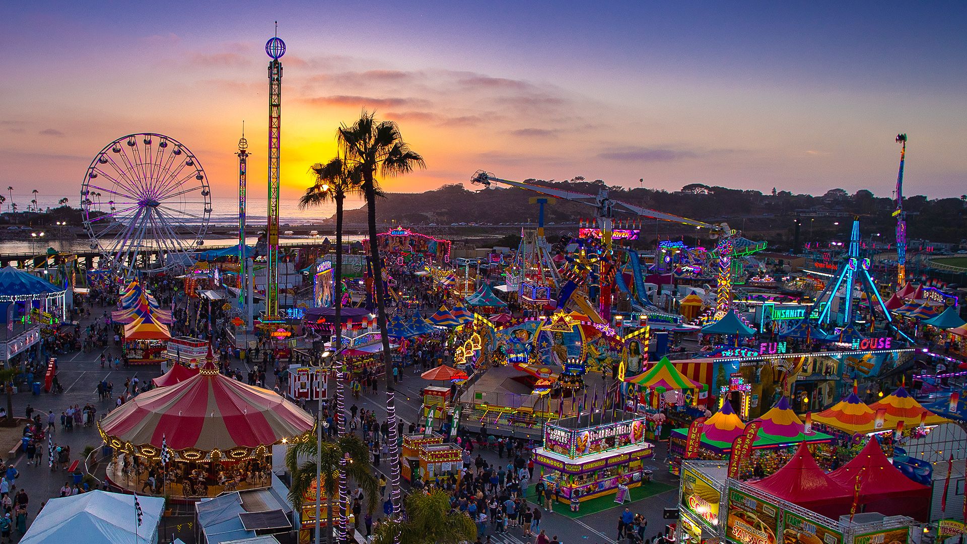 An aerial view of a county fair with colorful rides and games at sunset.