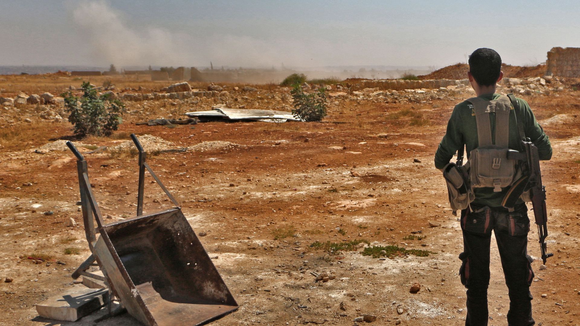A Syrian rebel fighter holding a gun looks out onto empty land.
