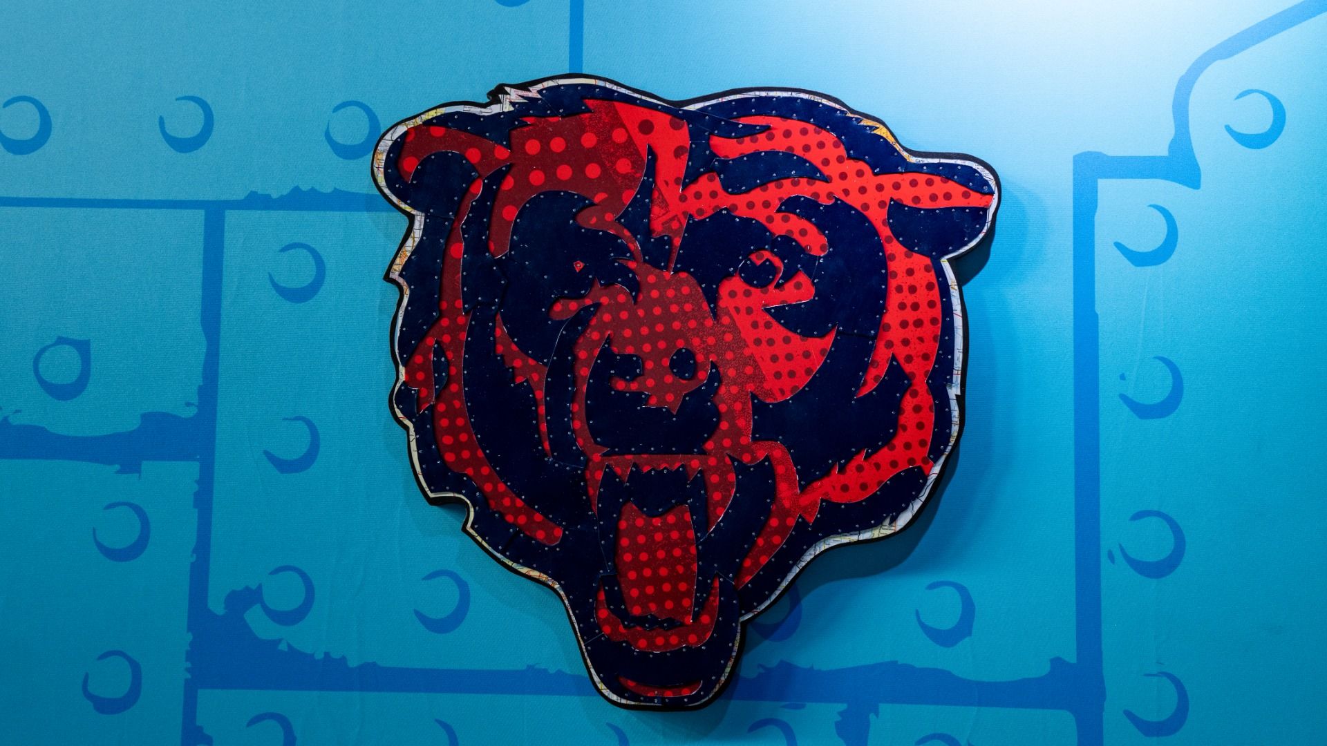 A large pop-art dragon head in red and dark blue with a dotted pattern, outlined in white, mounted on a bright blue wall with abstract geometric shapes and curved symbols in lighter blue.