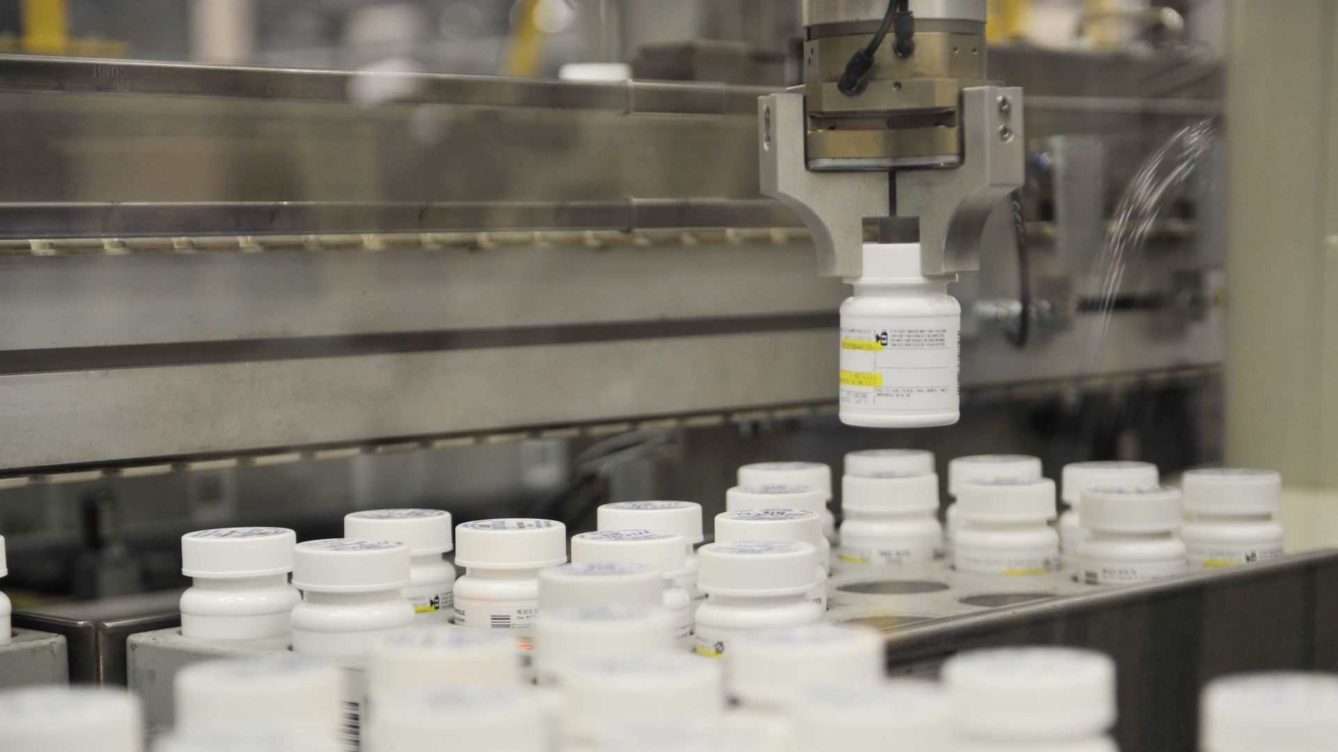A robot arm picks up a bottle of pills.