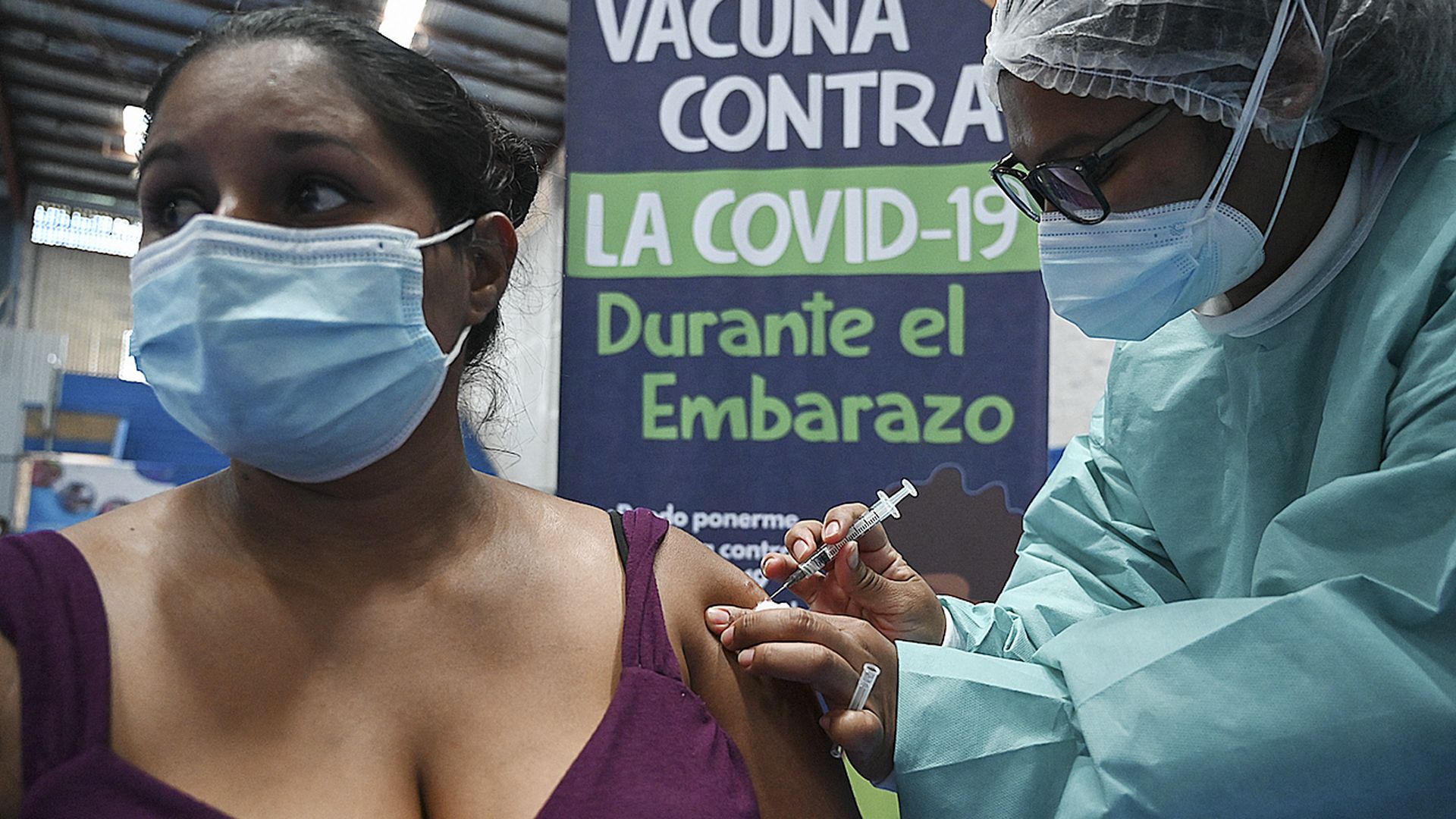 A woman wearing a mask receives a COVID-19 vaccine in the arm