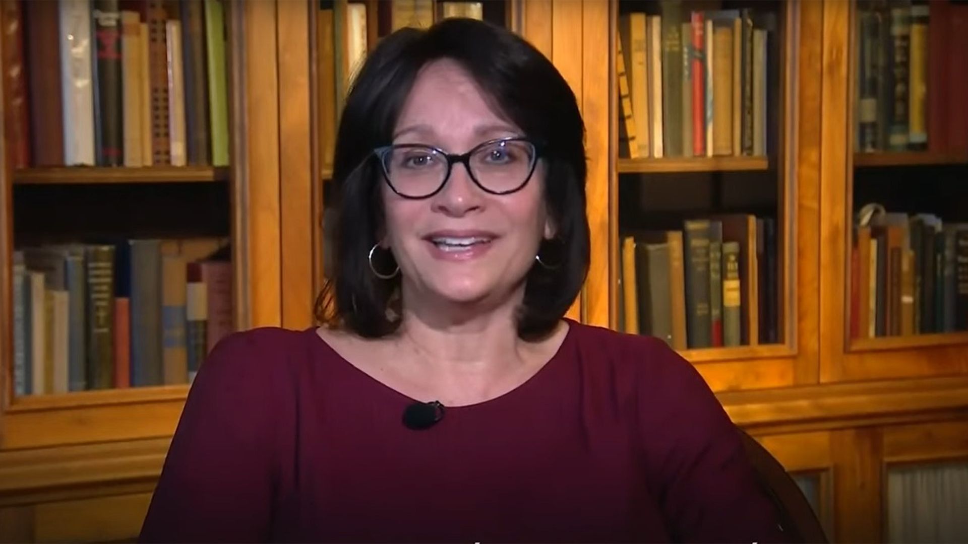 Author Meg Medina sits with a bookcase behind her 