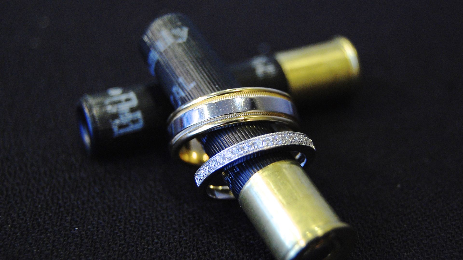 A black and gold colored shotgun shell with two wedding rings on it. 