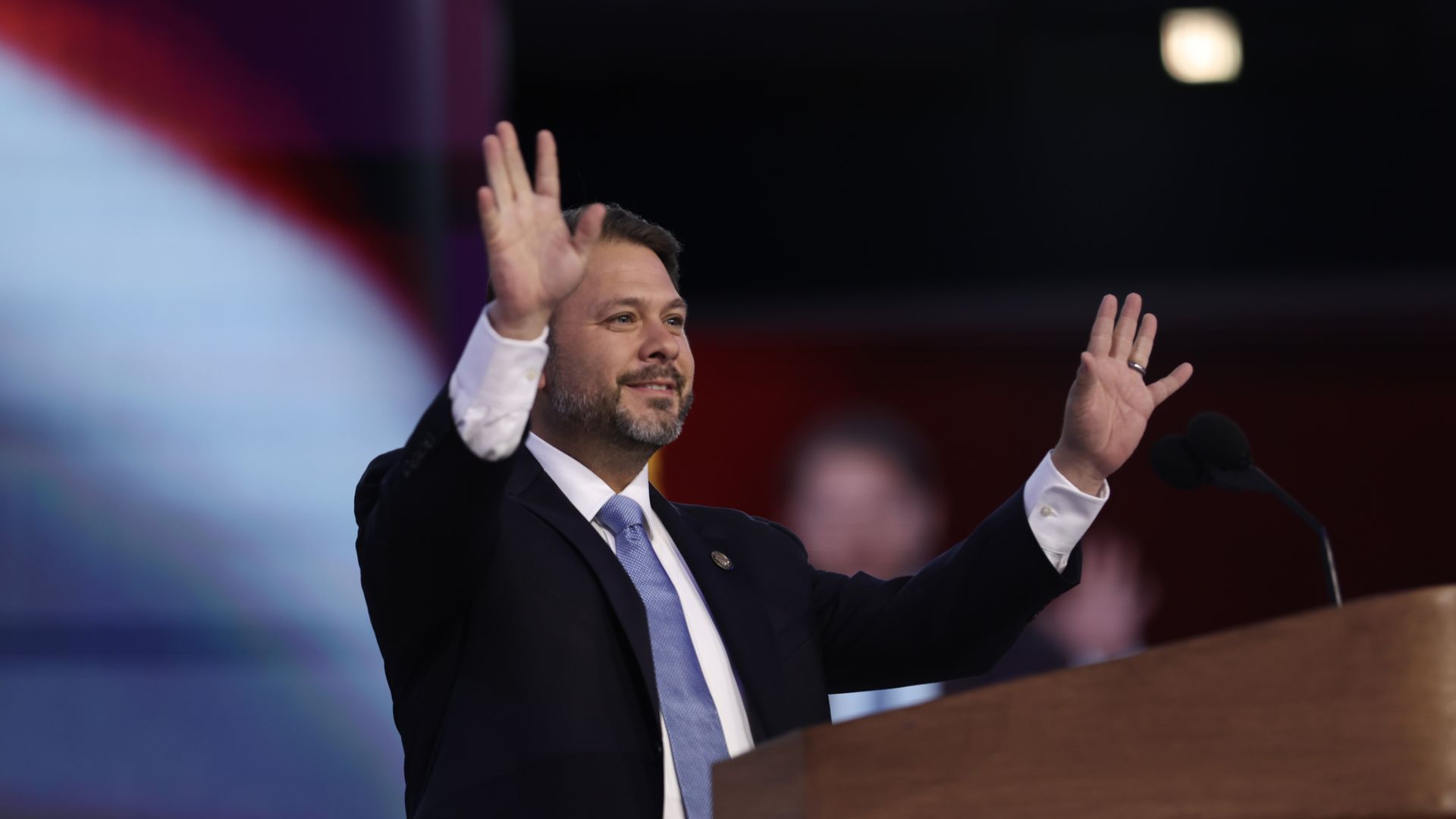 Ruben Gallego smiles and holds both hands in the air while standing behind a lectern on a stage.