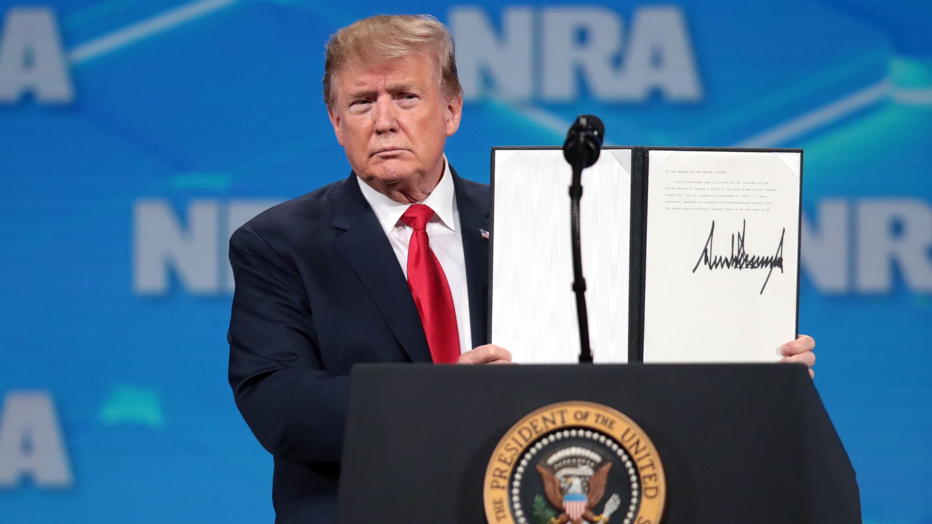 President Trump at lectern holding up signed document