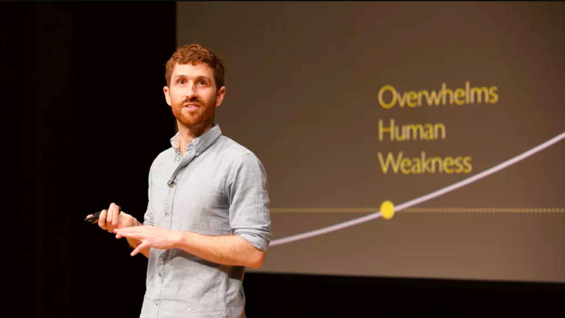 In this image, Tristan Harris stands and speaks on stage in a light colored casual dress shirt.