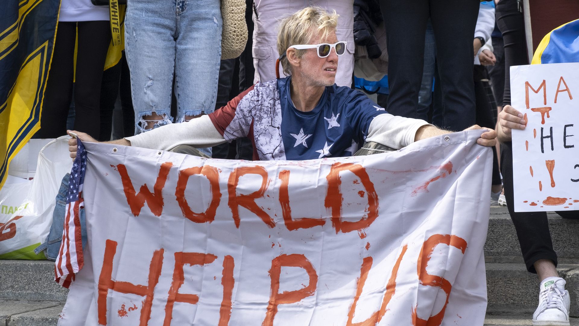 Ryan Routh holds a sign at a protest that says "WORLD HELP US" in red lettering.