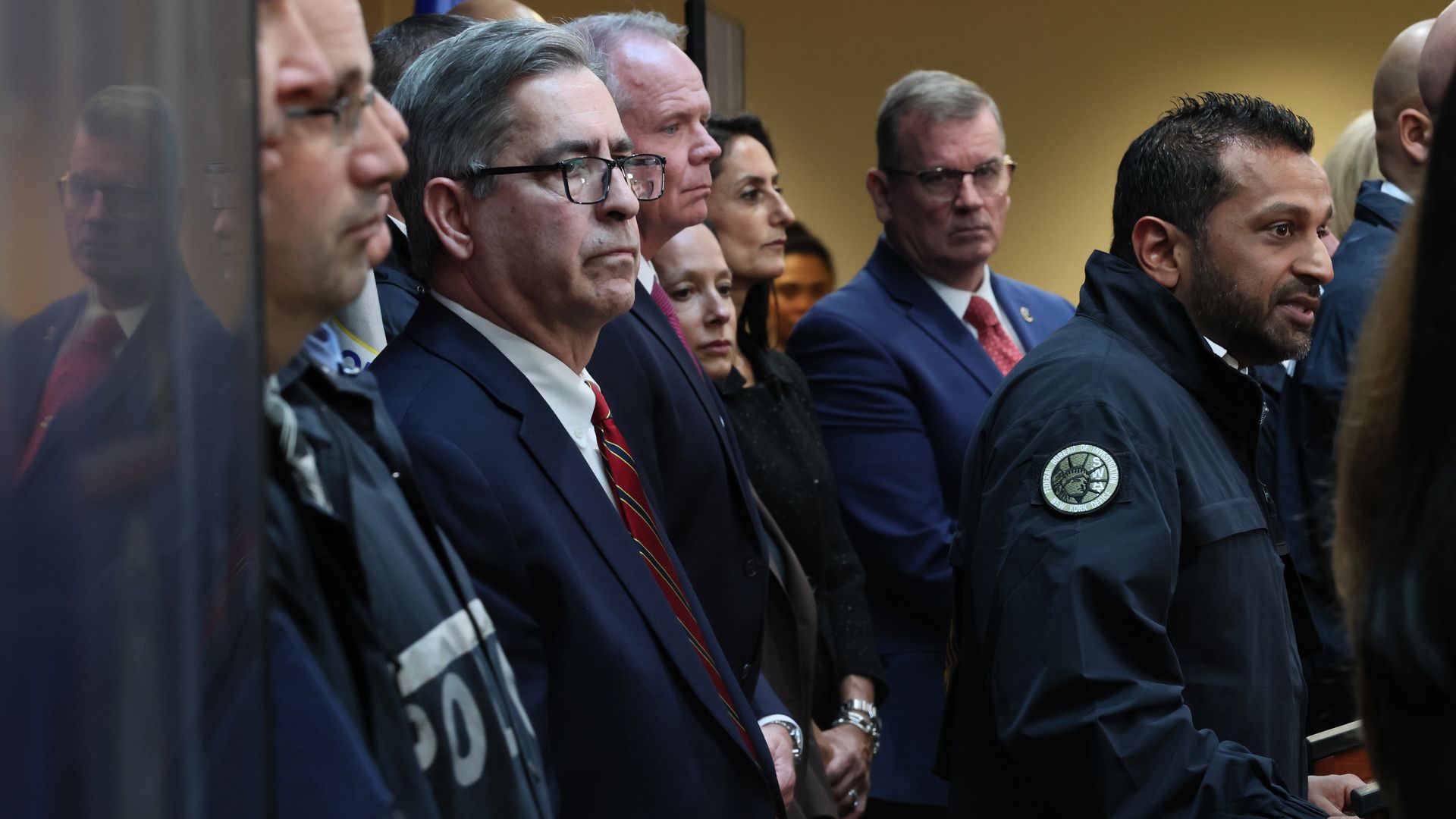 Several people in suits stand on a stage giving a press conference