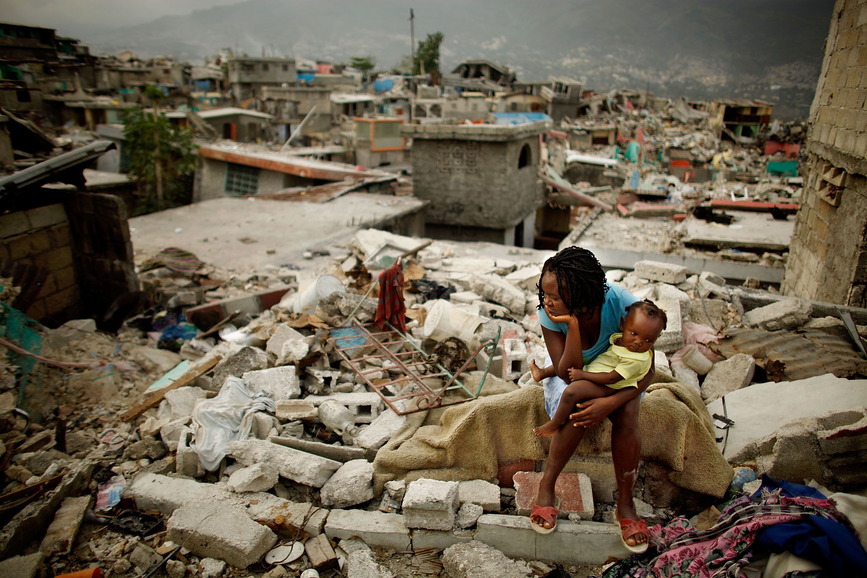 A woman and baby sit on the spot where her home collapsed during last month's 7.0 earthquake in the Fort National neighborhood February 26, 2010 in Port-au-Prince, Haiti.