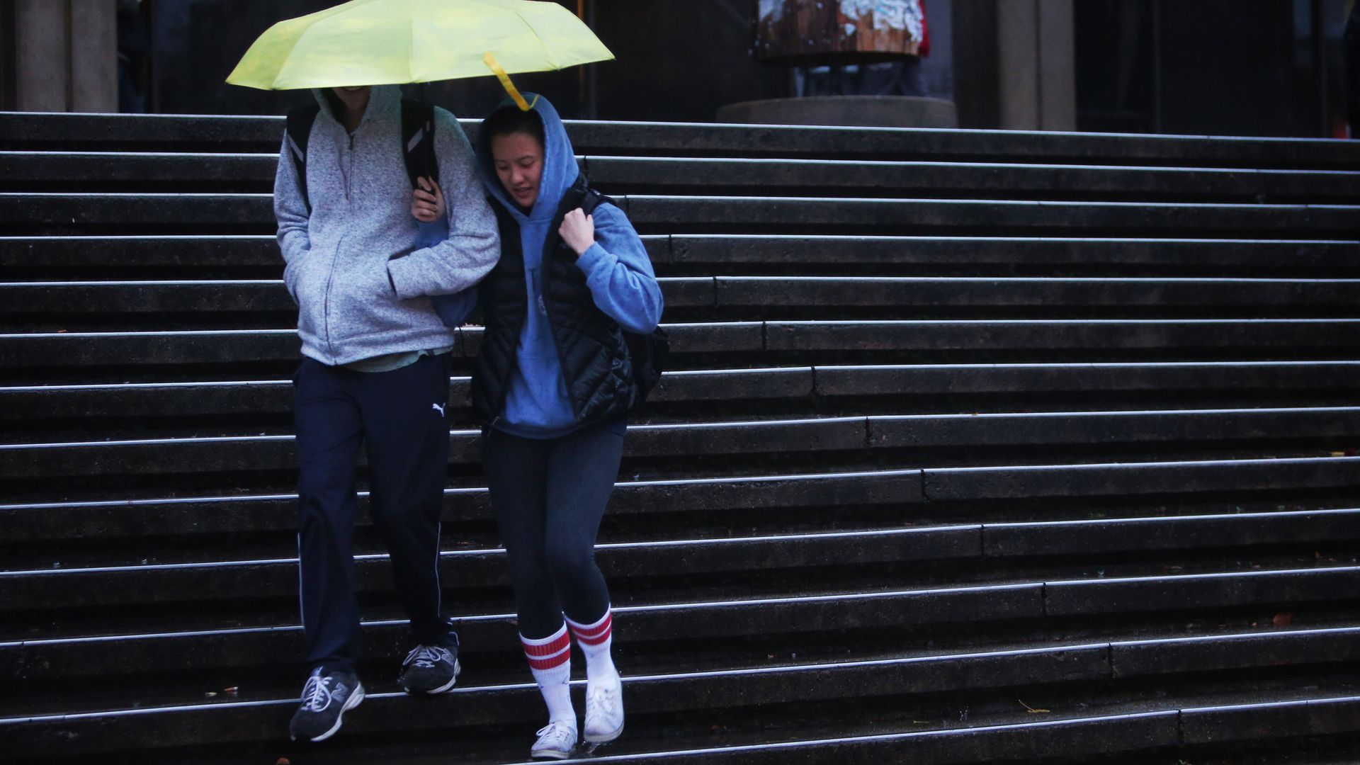 Two people walk down stairs sharing a lime green umbrella. 