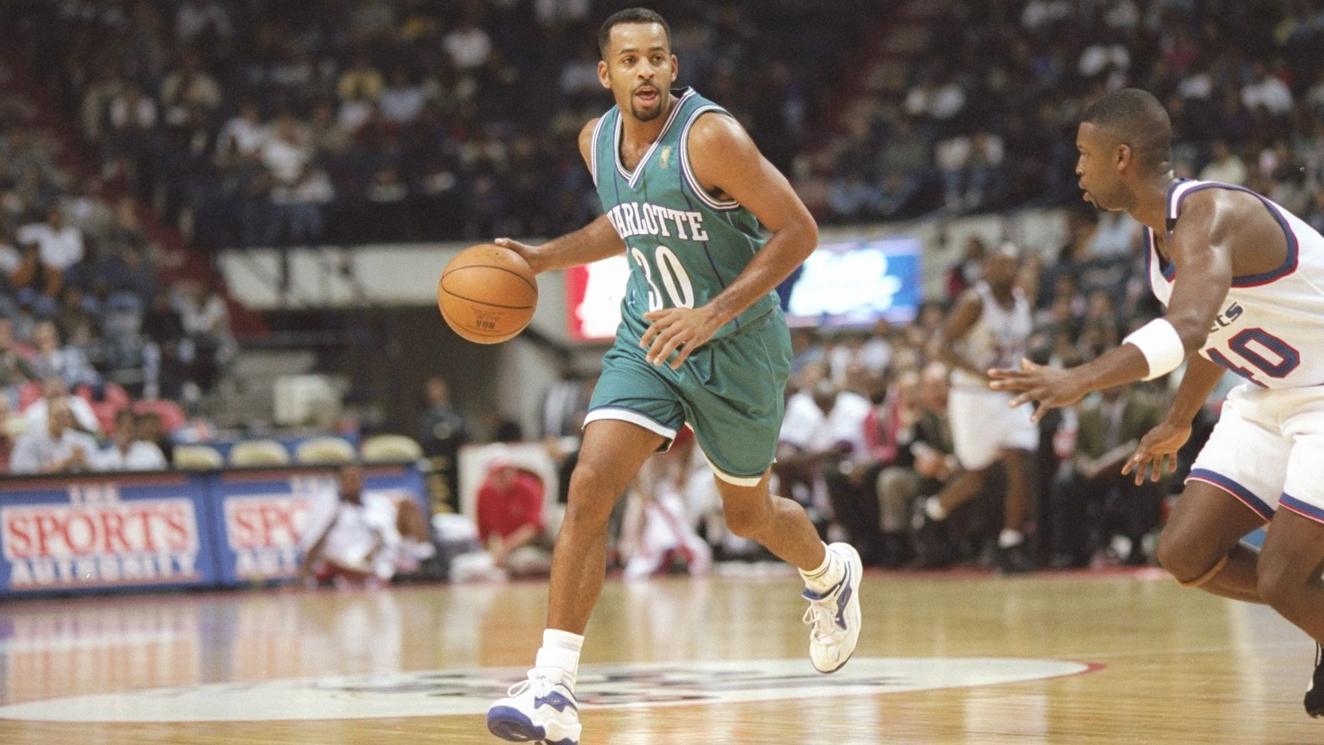 Dell Curry dribbling a basketball during a game in a purple and teal uniform. 