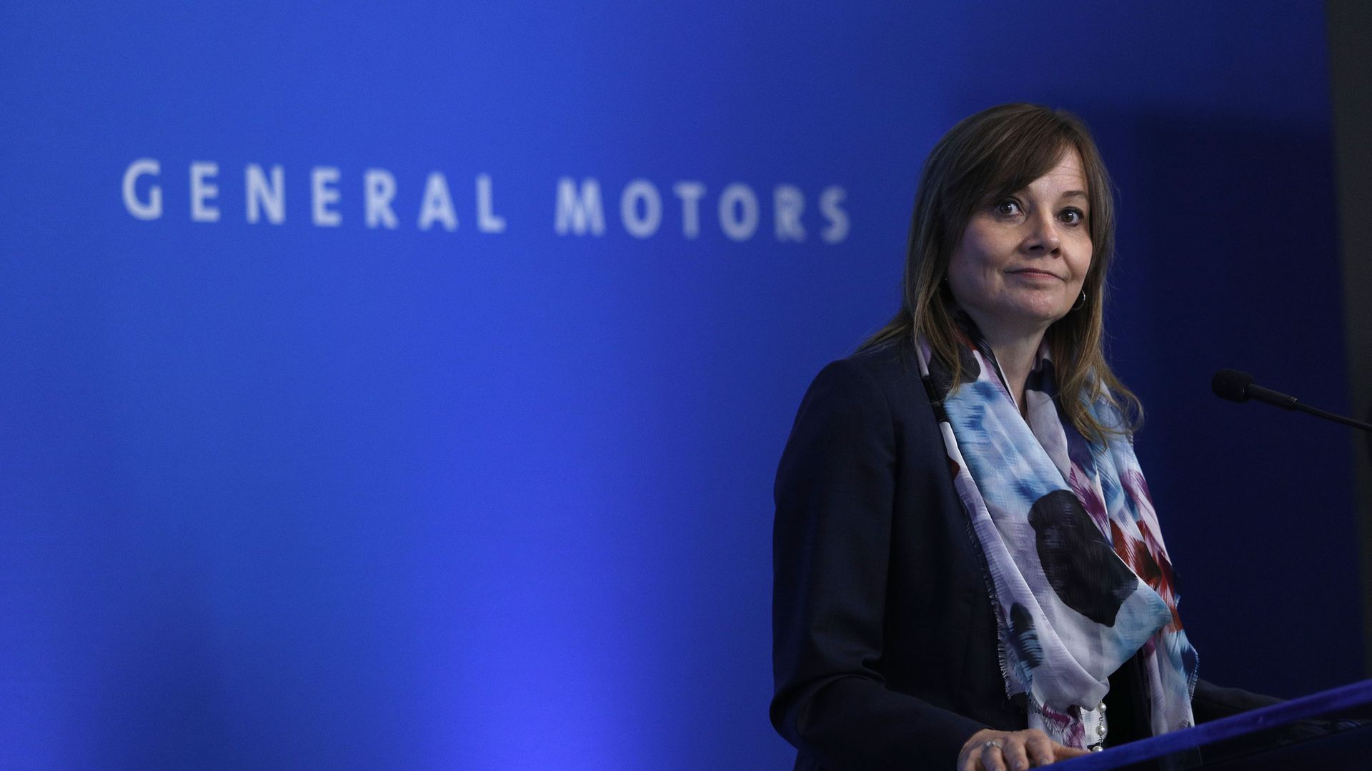  General Motors CEO Mary Barra speaks in front of a blue backdrop with white letters that spell "General Motors"