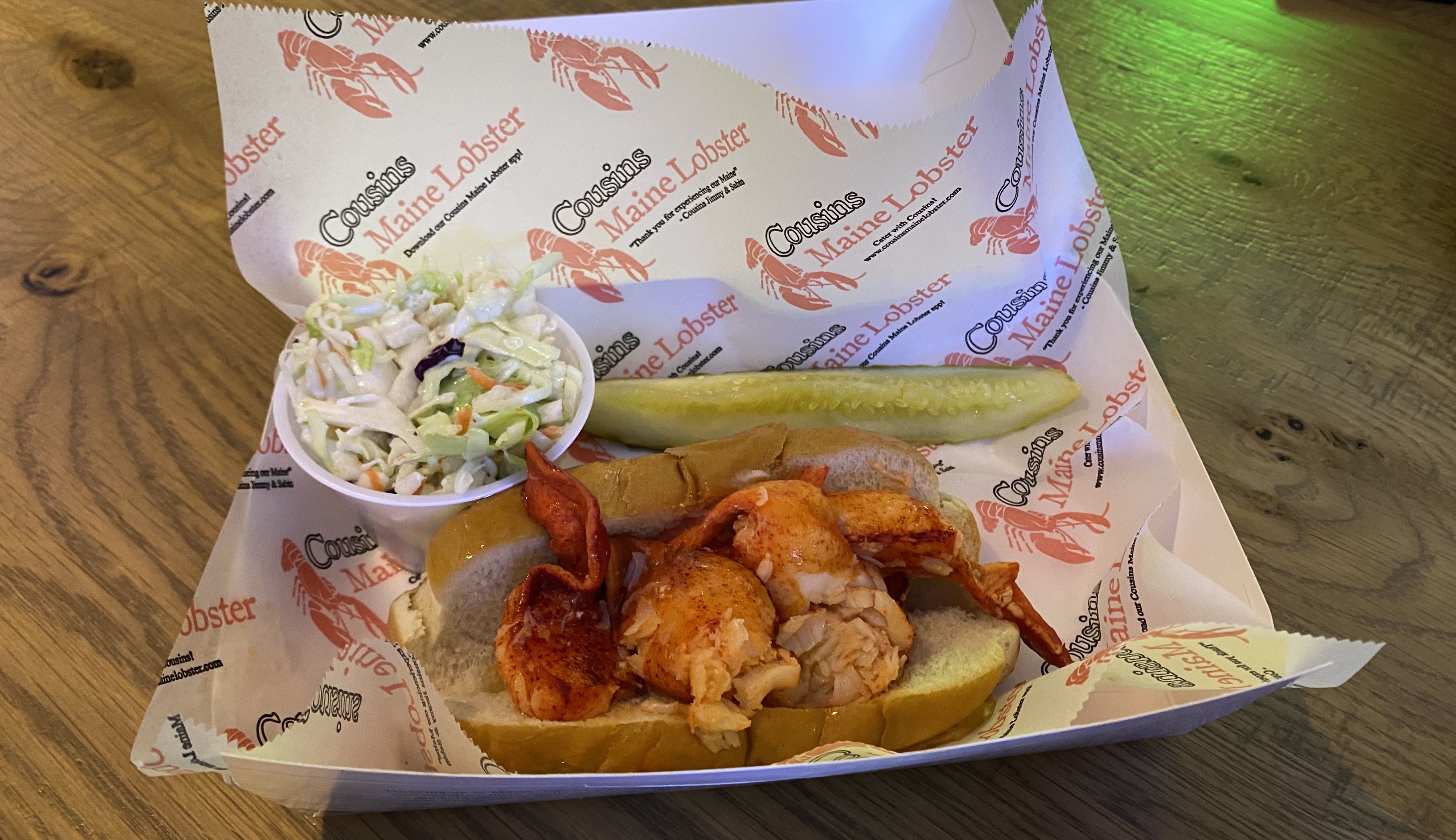 A lobster roll with coleslaw and a pickle spear