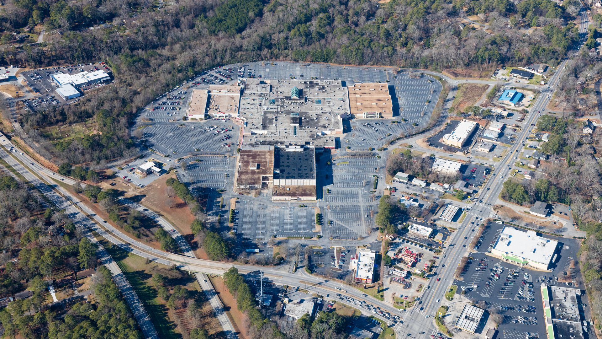 An aerial view of a typical 1960s enclosed shopping mall surrounded by parking lots and trees on the edges