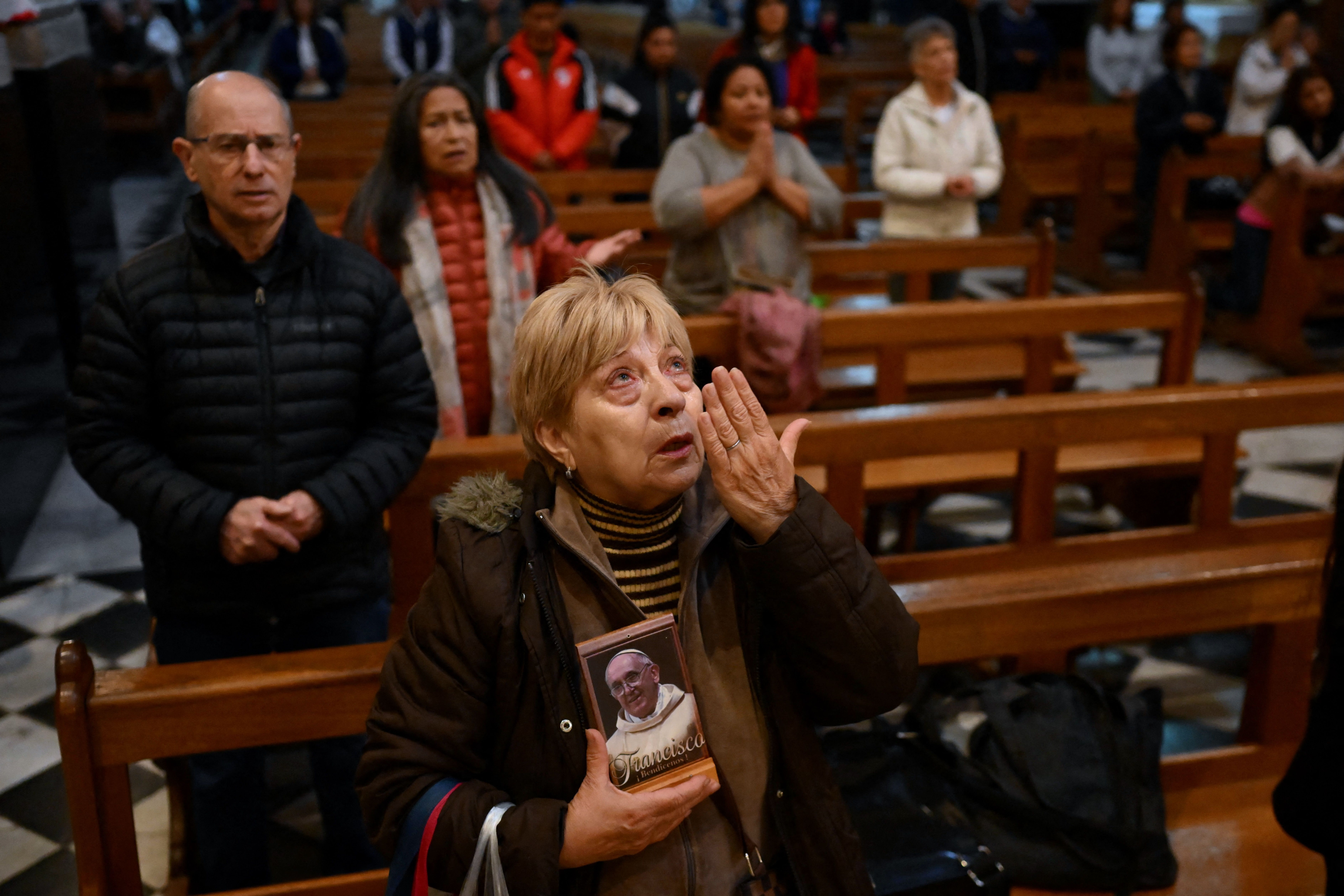 A woman prays holding a photo of Francis