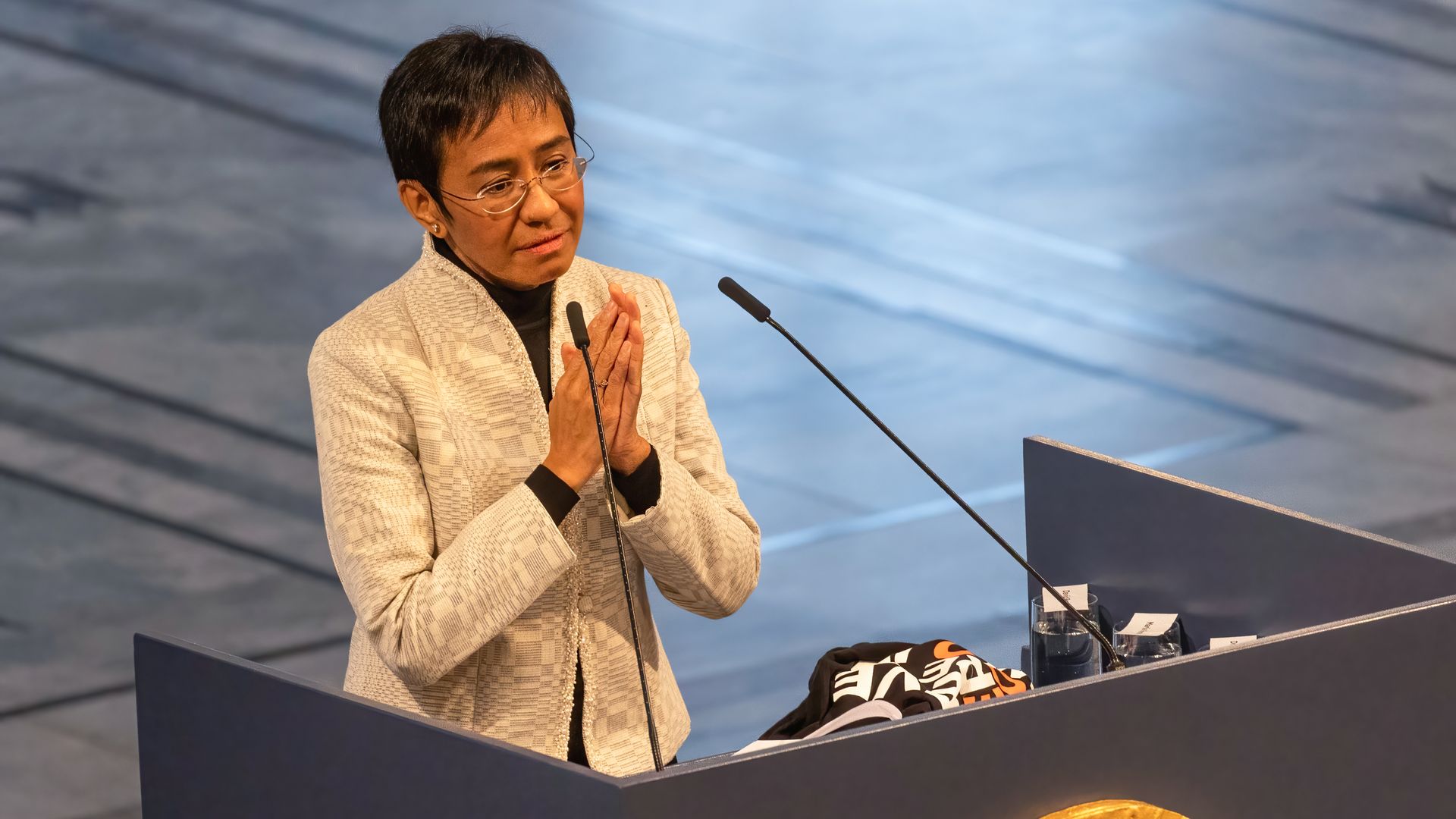A woman in a white suit clasps her hands together behind a lectern