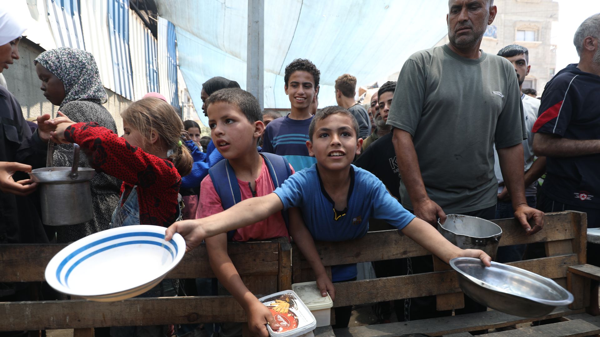Child holds out plates while other children and adults are around him