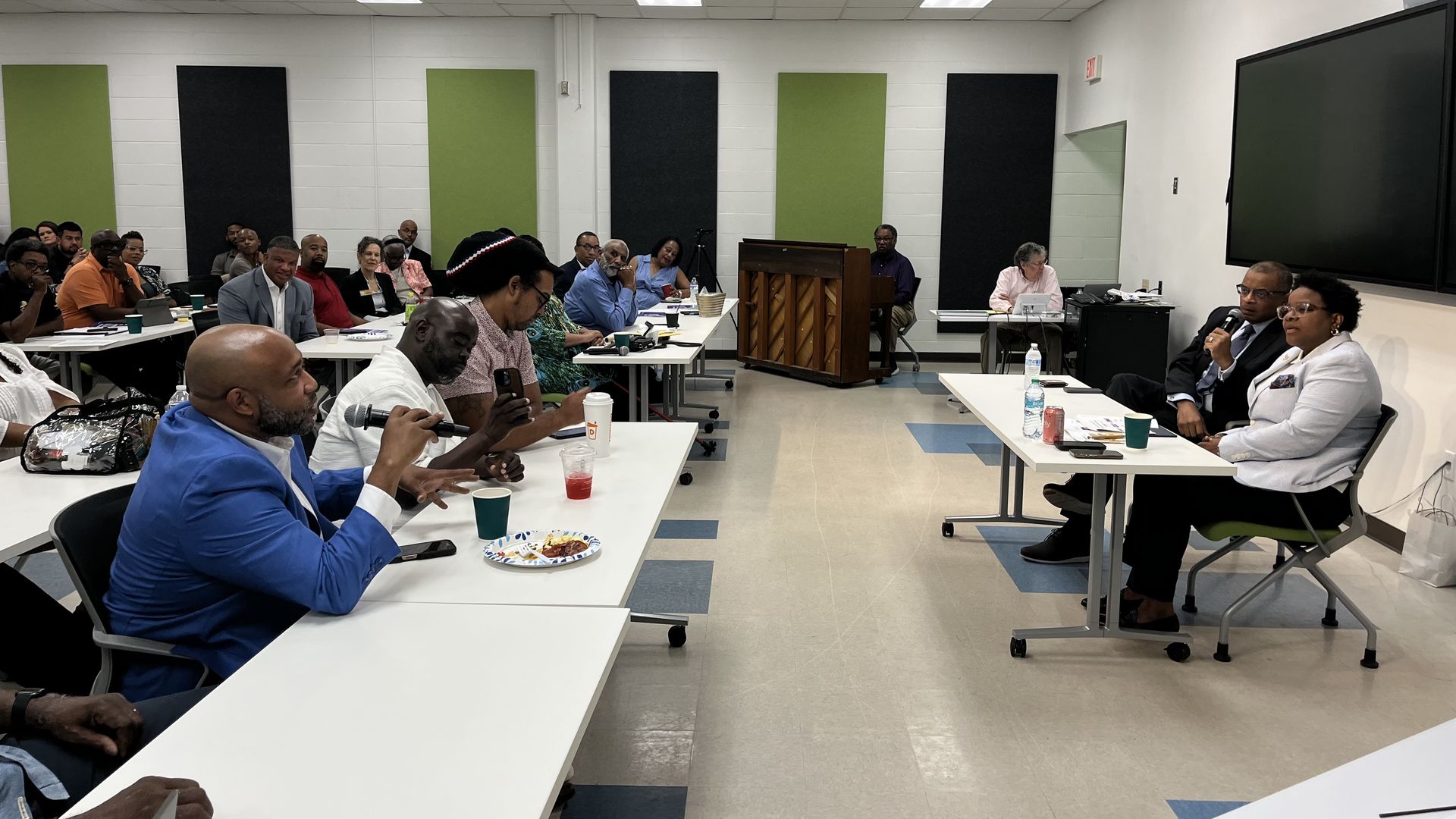 People hold microphones at tables during a public forum