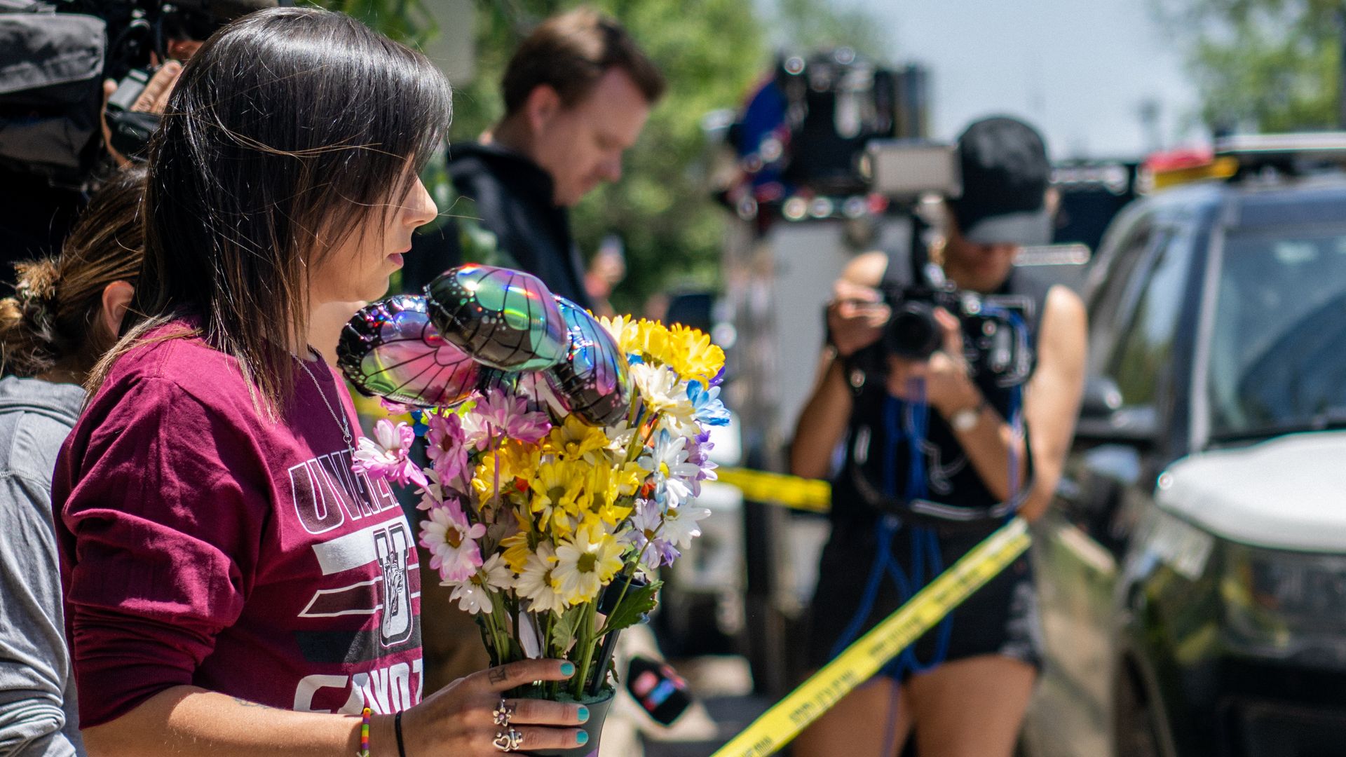 A woman is shown by the side holding a bouquet of yellow flowers and balloons at a memorial for the shooting victims in Uvalde, Texas