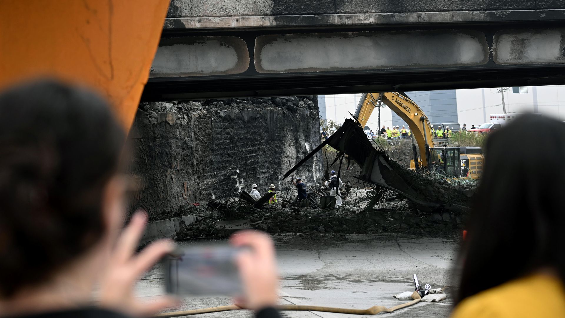 A person is shown taking a photo on his phone of the burned out bridge and wreckage