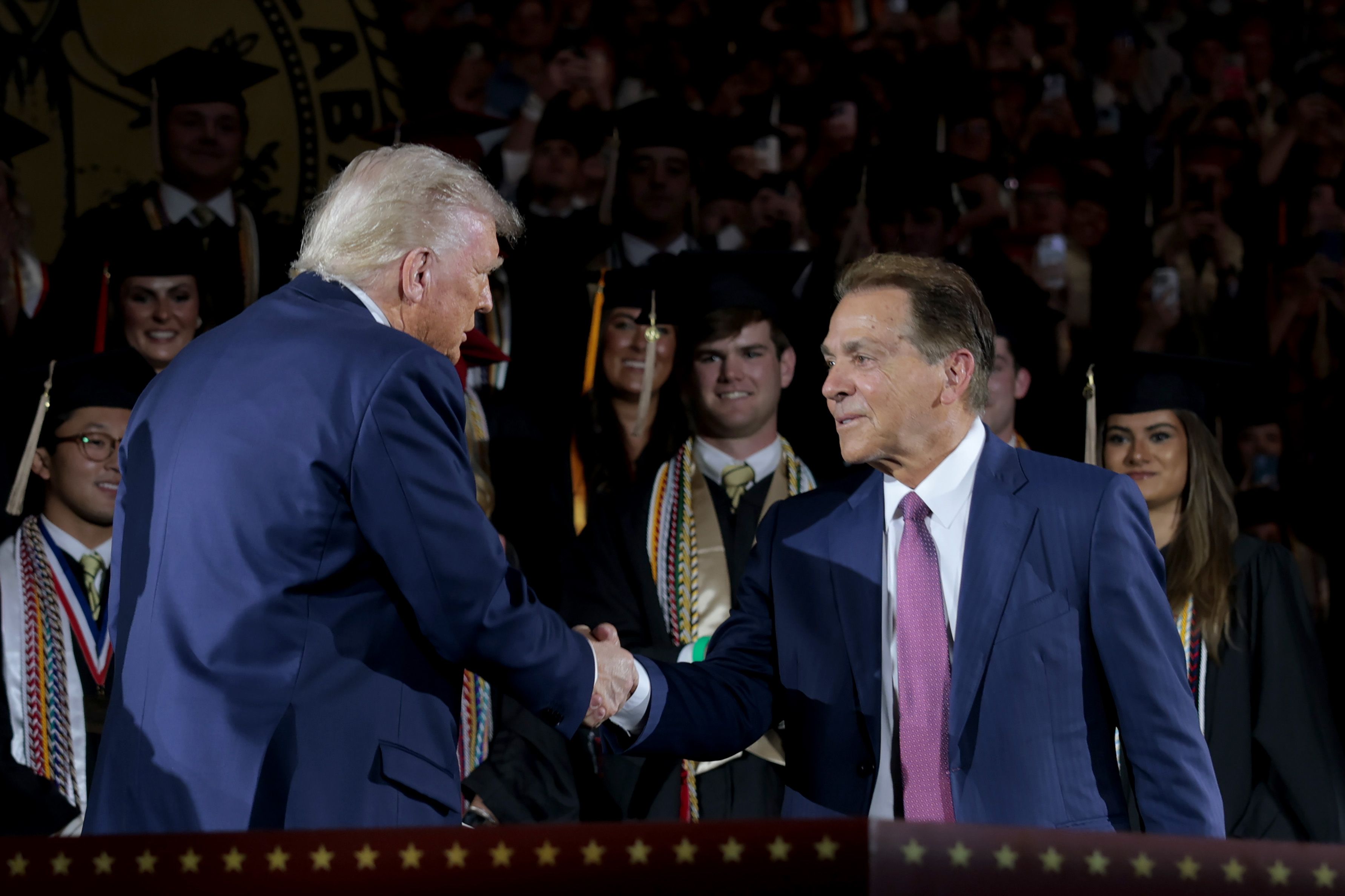 TUSCALOOSA, ALABAMA - MAY 01: U.S. President Donald Trump shakes hands with former Alabama Crimson Tide football coach Nick Saban as Trump takes the stage to address graduating students at Coleman Coliseum at the University of Alabama on May 01, 2025 in Tuscaloosa, Alabama. Trump's remarks come the 