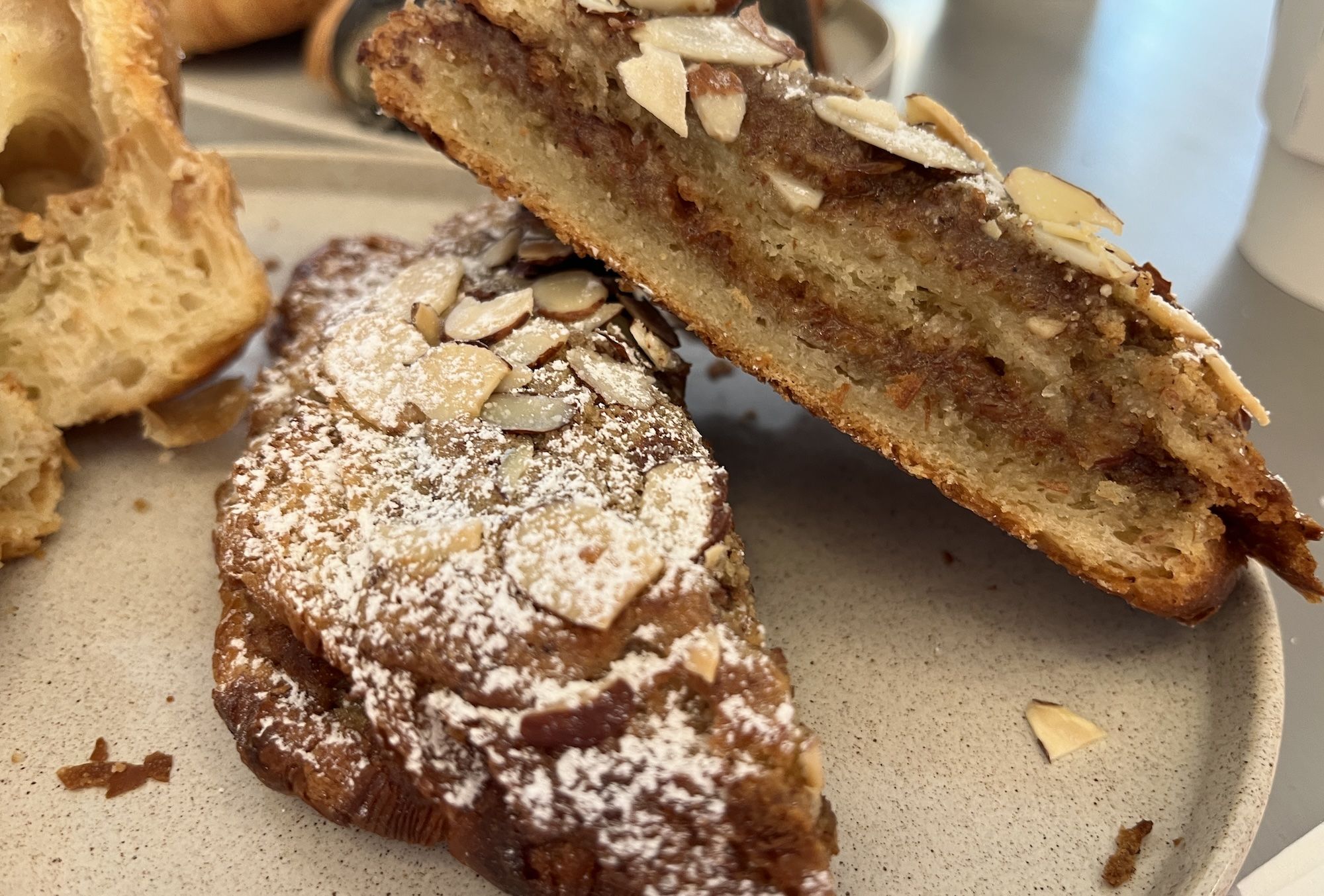 Close-up of a sliced almond cake on a plate, topped with almond slivers and a light dusting of powdered sugar; dense, nut-filled crumb with a golden-brown crust.