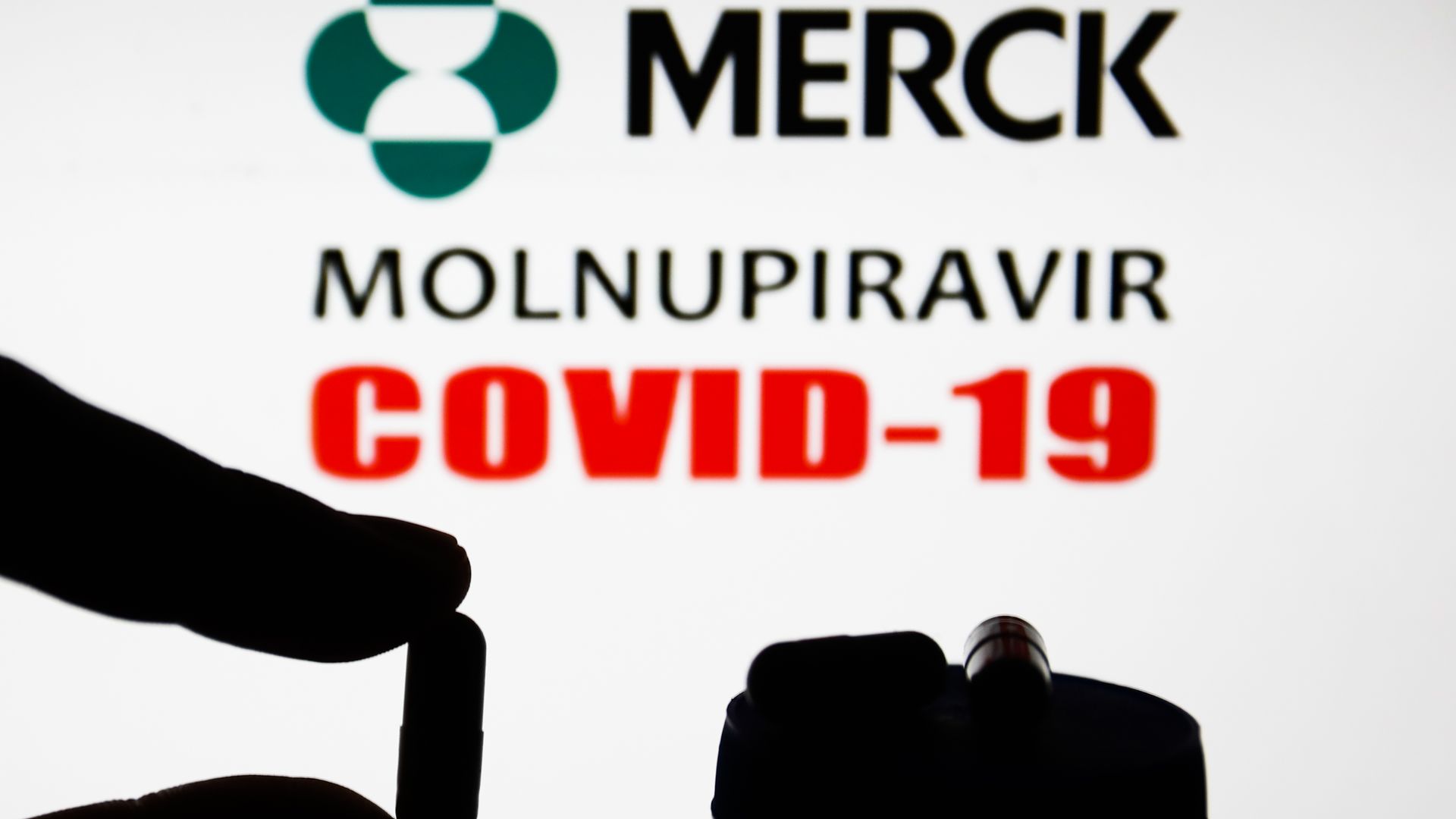 Medicine pill is seen with Merck logo and words 'Molnupiravir' and 'COVID-19' displayed on a screen in the background in this illustration photo .
