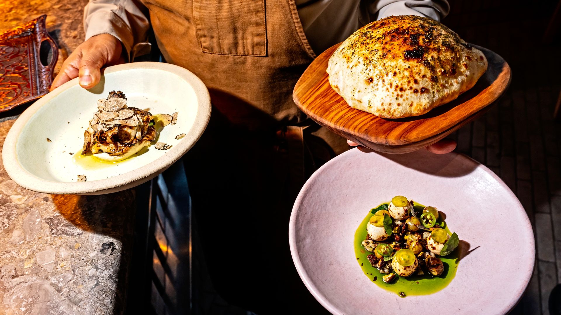 A chef holding two vegetable dishes and pita bread on three separate plates. 