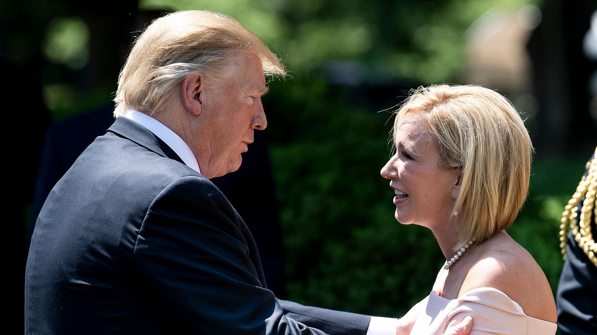 In this image, Trump and White hold each others' arms in a professional embrace while standing outside. 